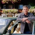 "Der Bergdoktor" - 18. Staffel: Vor der Arztpraxis: Dr. Martin Gruber (Hans Sigl) lehnt an der geöffneten Tür seines grünen Mercedes und lächelt in die Kamera.