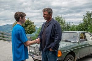 "Der Bergdoktor: Kindeswohl": Vor dem Haus der Familie Fischer: Vor dem grünen Mercedes stehen sich Dr. Martin Gruber (Hans Sigl) und John Luckau (Nico Marischka) gegenüber und reichen sich die Hände. Dr. Gruber lächelt den Jungen aufmunternd an.
