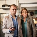 "Marie Brand und das tote Au-pair": Marie Brand (Mariele Millowitsch) und Jürgen Simmel (Hinnerk Schönemann) stehen in der Taxiwerkstatt Seifert und schauen beide zur Seite. Jürgen Simmel hat sein Handy in der Hand.