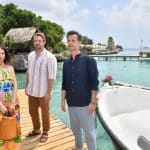 "Das Traumschiff: Curaçao": Am Meer: Neben einem Holzsteg liegt ein mit Blumen geschmücktes Boot. Auf dem Steg stehen Max Parger (Florian Silbereisen), Valerie Prinz (Nadine Menz) und Philipp Korte (David Korbmann). Traurig hält Valerie eine Tasche in den Händen.