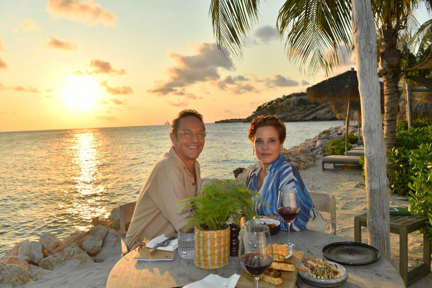 "Das Traumschiff: Curaçao": Bei Sonnenuntergang: An einem gedeckten Tisch am Strand sitzen Anna (Muriel Baumeister) und Konrad Thiele (Max Gertsch) nah beieinander und blicken glücklich in die Ferne.
