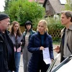 "Ein starkes Team - Der tote Mörder": Auf der Straße in einer Wohnsiedlung zeigt Linett (Stefanie Stappenbeck) Peter Perl (Steffen Groth) ein Schreiben der Staatsanwaltschaft. Beide sind im Gespräch und haben den Blick auf Otto (Florian Martens) gerichtet, der Peter zufrieden anlächelt. Im Hintergrund beobachten Karina (Joone Dankou) und Lotte (Sidney Fahlisch) die drei.