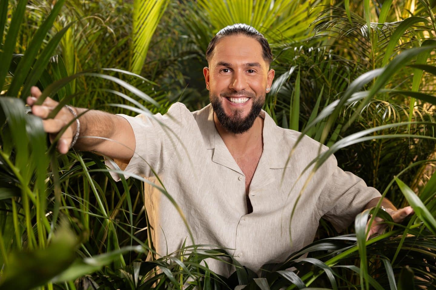 "Ich bin ein Star – Holt mich hier raus!": Wer fliegt, wer punktet? Der große Dschungelstar-Check von Jan Köppen! 2 Maurice Dziwak, lächelnd in einem beigefarbenen Hemd, mit zurückgekämmten Haaren und gepflegtem Bart, umgeben von tropischen Pflanzen im Dschungel.