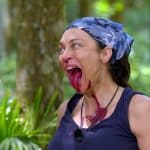 Lilly Becker während der Dschungelprüfung im Dschungelcamp. Mit weit aufgerissenem Mund und blutroten Essensresten im Gesicht zeigt sie ihre Entschlossenheit, die Prüfung zu meistern. Der grüne Dschungel im Hintergrund verstärkt die intensive Szenerie.
