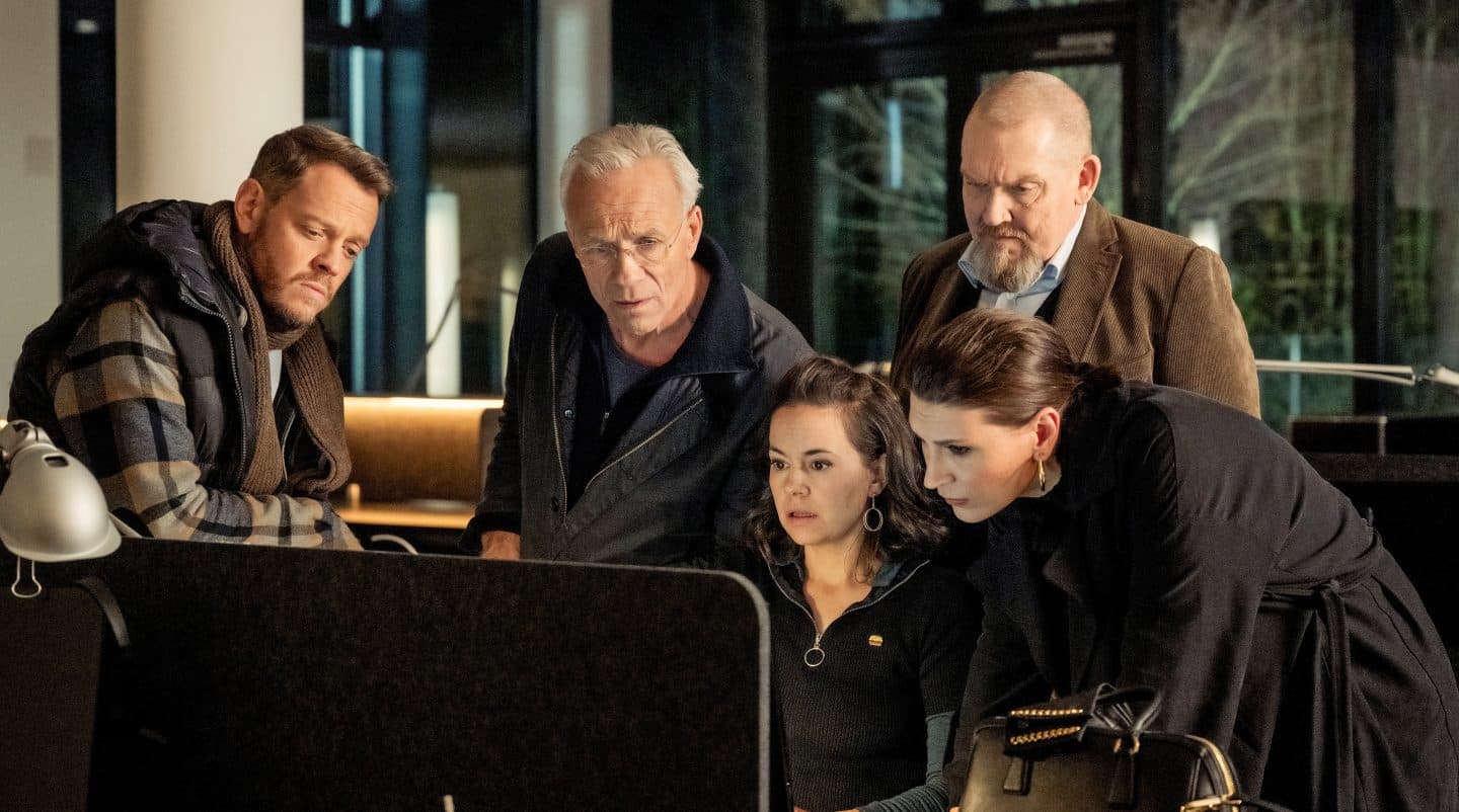 „Tatort: Restschuld“: Schuld, Blut und ein unsichtbares Opfer – Lohnt sich der neue Fall aus Köln? 3 Die Kommissare Norbert Jütte (Roland Riebeling), Max Ballauf (Klaus J. Behrendt) und Freddy Schenk (Dietmar Bär) stehen zusammen mit den Correct Inkasso-Managerinnen Silja Mayer (Karolina Horster) und Milena Ilic (Olga Prokot) vor einem Computerbildschirm. Alle blicken konzentriert auf die Daten, um Hinweise auf den brutalen Überfall auf den Mitarbeiter Fabian Pavlou zu finden. Die Szene zeigt die Ermittlungsarbeit und die Zusammenarbeit zwischen Polizei und Inkasso-Firma.