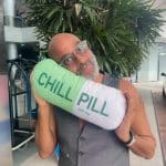 Pierre Sanoussi-Bliss hält ein Kissen in Form einer grünen Tablette mit der Aufschrift „CHILL PILL 100 mg“ an sein Gesicht.