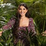 Yeliz Koç steht lächelnd inmitten dichter grüner Pflanzen. Sie trägt ein gemustertes, langärmliges Kleid und wirkt entspannt und selbstbewusst.