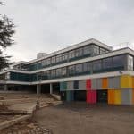 Das Friedrich-Schiller-Gymnasium in Marbach am Neckar. Das moderne Schulgebäude hat eine mehrstöckige Glas- und Fassadenkonstruktion mit bunten Farbakzenten an der unteren Etage. Eine breite Treppenanlage führt zum Haupteingang, während ein Baum im Vordergrund das Bild ergänzt. Der Himmel ist bewölkt.