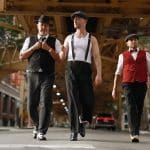 Drei Spitzenköche im Gangster-Look: Frank Rosin, Alexander Kumptner und Ali Güngörmüs laufen in eleganten Outfits durch eine Straße unter einer Hochbahnbrücke, inspiriert von der Al-Capone-Ära.