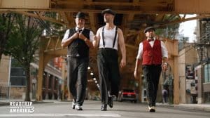 Drei Spitzenköche im Gangster-Look: Frank Rosin, Alexander Kumptner und Ali Güngörmüs laufen in eleganten Outfits durch eine Straße unter einer Hochbahnbrücke, inspiriert von der Al-Capone-Ära.