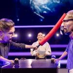 Joko Winterscheidt und Klaas Heufer-Umlauf tragen überdimensionale Masken und duellieren sich mit einem roten Schaumstoffstab, während Jeannine Michaelsen im Hintergrund moderiert. Die Szene spielt in einem bunten Studio mit futuristischer Beleuchtung.