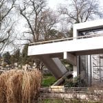 Das Schwingaffenhaus in der Wilhelma Stuttgart, ein Gebäude aus den 1970er-Jahren mit klaren Linien, großen Glasflächen und einem außenliegenden Treppenaufgang, umgeben von winterlichen Bäumen und trockenem Ziergras.