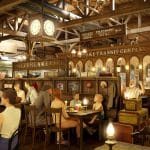 Illustration des neuen Western-Restaurants 'Diner Station' im Europa-Park: Eine detailreiche Darstellung im Stil eines alten Bahnhofs mit rustikaler Western-Atmosphäre, historischen Zugwaggons, stimmungsvoller Beleuchtung und thematisch gestalteten Sitzbereichen. Besucher erleben eine authentische Kulisse mit nostalgischen Elementen und Western-Dekoration.