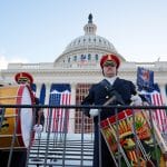 Zwei uniformierte Musiker der United States Army Band mit Trommel und Marschtrommel vor dem dekorierten Kapitol in Washington, das mit amerikanischen Flaggen geschmückt ist. Im Hintergrund ist die Kuppel des Kapitols zu sehen.