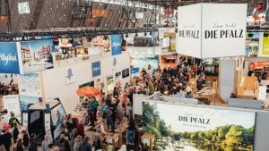 Eine belebte Messehalle der CMT in Stuttgart mit Ständen verschiedener Urlaubsregionen, darunter die Pfalz, das Allgäu und Bayern. Zahlreiche Besucher erkunden die Angebote der Aussteller.