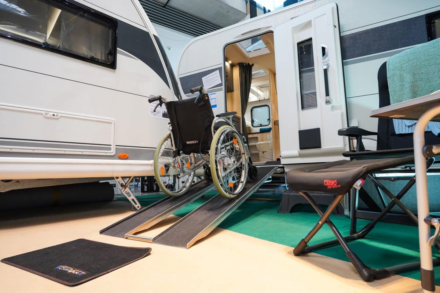 Ein Rollstuhl auf einer Rampe führt in einen speziell ausgestatteten, barrierefreien Wohnwagen auf der CMT 2025. Daneben stehen ein Campingstuhl und weitere Ausstellungsstücke.






