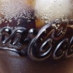 Ein gekühltes Glas Coca-Cola mit Eiswürfeln. Das Glas ist mit Kondenswasser bedeckt, und das bekannte Coca-Cola-Logo ist in das Glas eingeprägt.