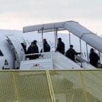 Polizeibeamte begleiten Personen an Bord eines Flugzeugs am Baden-Airpark. Die Szene zeigt eine Abschiebung mit Sicherheitskräften, während mehrere Personen über eine Gangway das Flugzeug betreten. Das Flugzeug trägt die Farben einer ausländischen Fluggesellschaft.