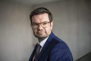 Marco Buschmann, designierter FDP-Generalsekretär, im Porträt. Er trägt einen dunkelblauen Anzug, ein weißes Hemd und eine gemusterte Krawatte, dazu eine Brille. Sein Blick ist nachdenklich, im Hintergrund ist eine schlichte Wand unscharf zu erkennen.