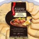 Verpackte Käseplatte mit in Scheiben geschnittenem Morbier-Raclettekäse mit Senfkörnern. Die Verpackung trägt die Aufschrift „Assiette pour Raclette“ und zeigt ein Bild mit geschmolzenem Käse, Aufschnitt und Beilagen. Hergestellt in der Region Franche-Comté, Frankreich.