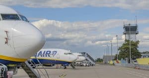 Zwei Ryanair-Flugzeuge stehen auf dem Rollfeld des Flughafens Karlsruhe/Baden-Baden vor einem Kontrollturm, bei klarem Himmel mit einigen Wolken. Im Hintergrund sind Flughafeninfrastruktur und Bäume zu sehen.