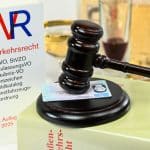Symbolbild zum Thema Straßenverkehrsrecht und Alkoholkonsum: Ein Gesetzesbuch zum Straßenverkehrsrecht, ein Richterhammer auf einem Führerschein sowie alkoholische Getränke im Hintergrund. Darstellung rechtlicher Konsequenzen bei Alkohol am Steuer.