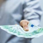 Eine Hand, die mehrere 100-Euro-Scheine hält, symbolisiert die Auszahlung von Geld oder einer Prämie.
