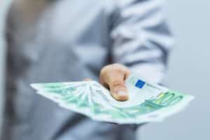 Eine Hand, die mehrere 100-Euro-Scheine hält, symbolisiert die Auszahlung von Geld oder einer Prämie.