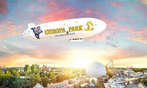 Illustration: Der Europa-Park Zeppelin mit dem Jubiläumslogo 2025 fliegt über den Freizeitpark, umgeben von einer malerischen Abendstimmung mit Achterbahnen und der markanten Kuppel im Hintergrund.