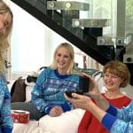 MrBeast macht seiner Freundin Thea einen Heiratsantrag. Er kniet auf einem weißen Teppich und präsentiert eine Ringbox, während Thea lächelt. Im Hintergrund sitzen zwei Frauen, darunter vermutlich Familienmitglieder, die den Moment freudig beobachten.