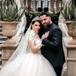 Reality-Star Cosimo Citiolo und seine Verlobte Nathalie Gaus in eleganter Hochzeitskleidung vor einer prächtigen Treppe in Italien. Die beiden blicken in die Kamera, während sie sich festhalten – ein Moment voller Romantik und Spannung.