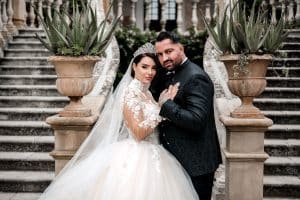 Reality-Star Cosimo Citiolo und seine Verlobte Nathalie Gaus in eleganter Hochzeitskleidung vor einer prächtigen Treppe in Italien. Die beiden blicken in die Kamera, während sie sich festhalten – ein Moment voller Romantik und Spannung.