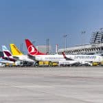 Mehrere Flugzeuge verschiedener Airlines, darunter Turkish Airlines und Pegasus, stehen nebeneinander auf dem Vorfeld des Flughafens Stuttgart vor einem modernen Terminalgebäude. Der Himmel ist klar und blau.