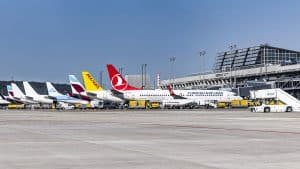 Mehrere Flugzeuge verschiedener Airlines, darunter Turkish Airlines und Pegasus, stehen nebeneinander auf dem Vorfeld des Flughafens Stuttgart vor einem modernen Terminalgebäude. Der Himmel ist klar und blau.