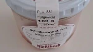Ein Glas Schinkenwurst der Marke Metzgerei Nießlbeck. Auf dem Etikett sind Produktdetails wie die PLU 881, ein Füllgewicht von 180 Gramm und das Mindesthaltbarkeitsdatum 28.12.2025 zu sehen.