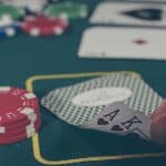 Ein Pokertisch mit grünem Filz, darauf rote Pokerchips und ein Spieler, der zwei Karten hält, ein Ass und einen König in Herz. Im Hintergrund unscharf weitere Chips und Karten, die die Casino-Atmosphäre unterstreichen.