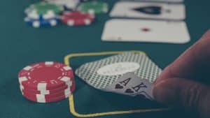 Ein Pokertisch mit grünem Filz, darauf rote Pokerchips und ein Spieler, der zwei Karten hält, ein Ass und einen König in Herz. Im Hintergrund unscharf weitere Chips und Karten, die die Casino-Atmosphäre unterstreichen.