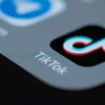 Ein Smartphone-Bildschirm mit verschiedenen App-Symbolen, darunter prominent das TikTok-Logo in Schwarz mit dem charakteristischen Musiknoten-Symbol. Der Hintergrund ist dunkel, wodurch die Apps hervorgehoben werden.