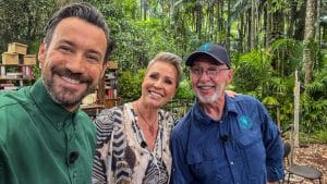 Die Moderatoren Jan Köppen und Sonja Zietlow zusammen mit Dr. Bob im Dschungelcamp. Sie lächeln in die Kamera, während im Hintergrund der typische Dschungel-Set-Aufbau mit Büchern und Kisten zu sehen ist.
