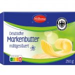 Verpackung der Milbona Deutsche Markenbutter (mildgesäuert, 250 g). Die Verpackung ist überwiegend blau und grün gestaltet, mit dem Milbona-Logo in Rot oben rechts. Ein Siegel mit dem Bundesadler weist auf geprüfte Markenqualität hin. Im Vordergrund sind dekorativ gerollte Butterflocken auf einer Brotscheibe abgebildet. Der Nutri-Score ist mit E gekennzeichnet.