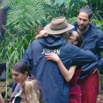 Jürgen Hingsen verabschiedet sich im Dschungelcamp von Lilly Becker mit einer innigen Umarmung. Maurice Dziwak steht daneben und beobachtet die Szene. Im Hintergrund sind weitere Camp-Bewohner sowie tropische Vegetation zu sehen.