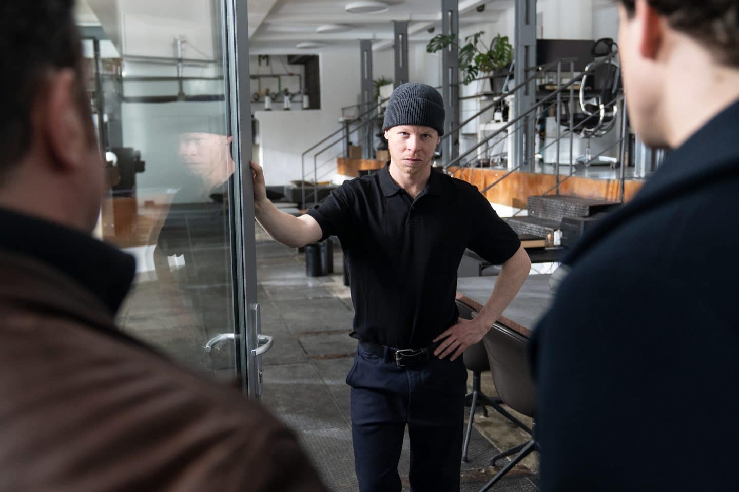 "Die Chefin - Fake News": Mit einer Hand an seiner offenen Haustür aus Glas blickt Robert Zeckler (Martin Wißner) seinen Besuch ernüchtert an. Das Innere der Wohnung ist loftartig. Zwei Hinterköpfe sind vor der Glastür.
