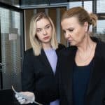 "Die Chefin - Fake News": Tanja Meineke (Anna Herrmann) sieht Vera Lanz (Katharina Böhm) von der Seite an, während Lanz mit Gummihandschuh ein Papier in der Hand hält. Sie befinden sich in einem Büroraum.