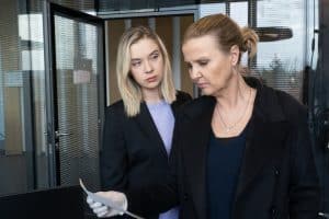 "Die Chefin - Fake News": Tanja Meineke (Anna Herrmann) sieht Vera Lanz (Katharina Böhm) von der Seite an, während Lanz mit Gummihandschuh ein Papier in der Hand hält. Sie befinden sich in einem Büroraum.