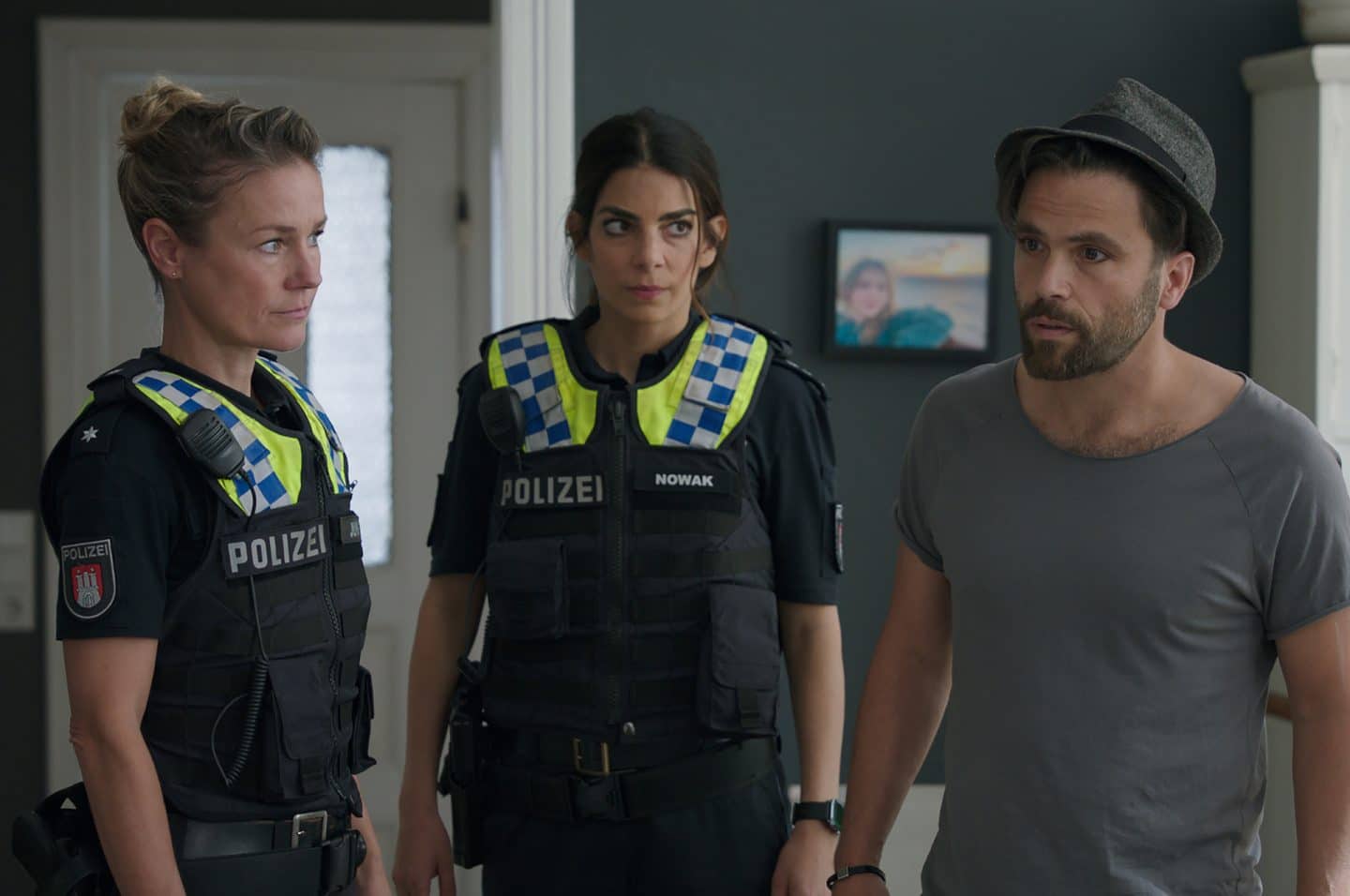 "Notruf Hafenkante - Ausgebrannt": Die Polizistinnen Franzi Jung (Rhea Harder-Vennewald) und Isa Nowak (Lilli Hollunder) stehen nebeneinander in einem Wohnraum. Beide schauen zu Rami Leyd (Karim Cherif), der neben ihnen steht. Er schaut nachdenklich ins Leere.
