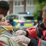 "Notruf Hafenkante - Kein Zurück": Großaufnahme von Dr. Haase (Fabian Harloff) und Julia Jacobi (Inga Lessmann). Dr. Haase versorgt Julia Jacobi, die auf einer Patiententrage liegt, daneben stehen zwei Sanitäter (Komparsen). Im Hintergrund steht ein Streifenwagen.
