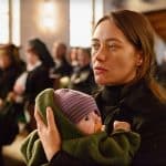 "Spreewaldkrimi - Böses muss mit Bösem enden": Fina Jurisch (Mercedes Müller) sitzt in einer Kirche und hat ihr Baby auf ihrem Schoß. Im Hintergrund sitzen weitere Personen (Komparsen) in Kirchenbänken.