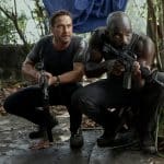 "Plane - Absturz im Dschungel": Brodie Torrance (Gerard Butler) und Louis Gaspare (Mike Colter) hocken auf einem Zementboden im Dschungel und haben ihre Waffen im Anschlag.