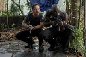 "Plane - Absturz im Dschungel": Brodie Torrance (Gerard Butler) und Louis Gaspare (Mike Colter) hocken auf einem Zementboden im Dschungel und haben ihre Waffen im Anschlag.