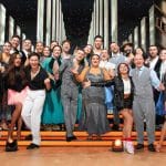 Gruppenfoto der 'Let's Dance'-Kandidaten auf der Bühne. Die Promis und Profis posieren gemeinsam in eleganten Outfits, viele lächeln und zeigen jubelnde Gesten. Im Hintergrund ist das festlich beleuchtete Show-Set zu sehen.